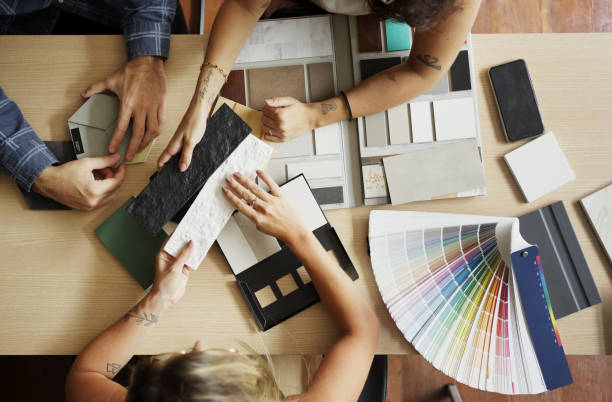 Вид сверху на творческую группу, обсуждающую образцы материалов и образцы цветов на деревянном столе в офисной обстановке.